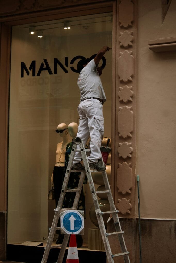 Worker on a ladder renovating the facade of a storefront, enhancing store aesthetics.